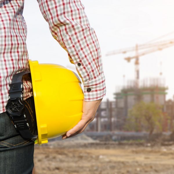 Hand’s engineer worker holding yellow safety helmet with buildin